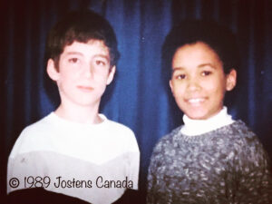 This image is of two former classmates of Woodland School in Verdun, early 1989. In front of the blue curtain backdrop is Todd - on the left wearing a white, gray and black chevron sweater, and Li - on the right wearing a white turtleneck and a blended dark grey and white sweater. This is part of a school photo, credited to Jostens Canada.